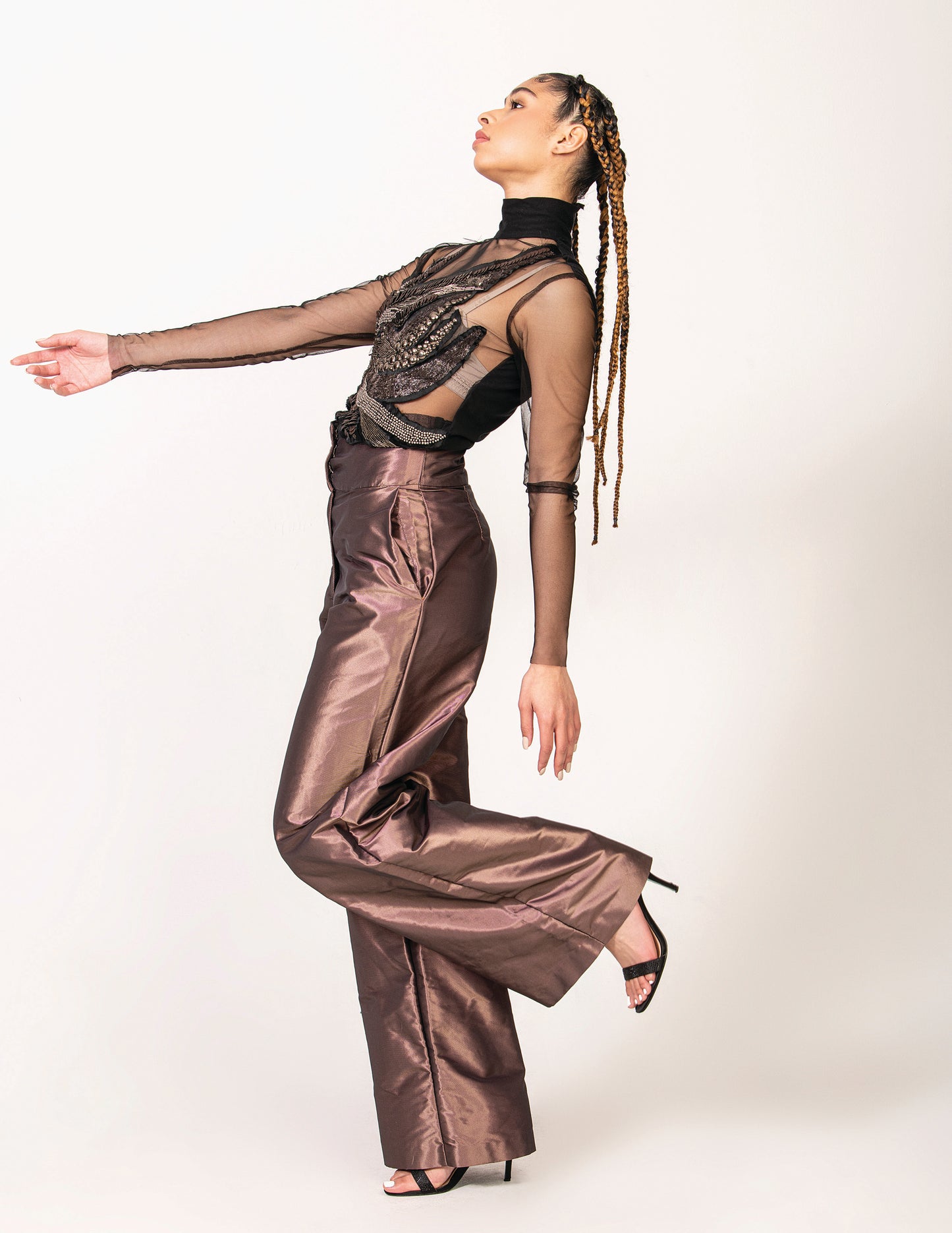 Woman posing with sheer black leather and metallic embroidered top with high heels and metallic purple pants