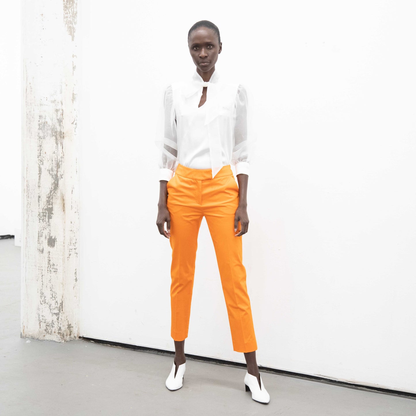 Woman wearing a white silk blouse with integrated bow neck over orange pants