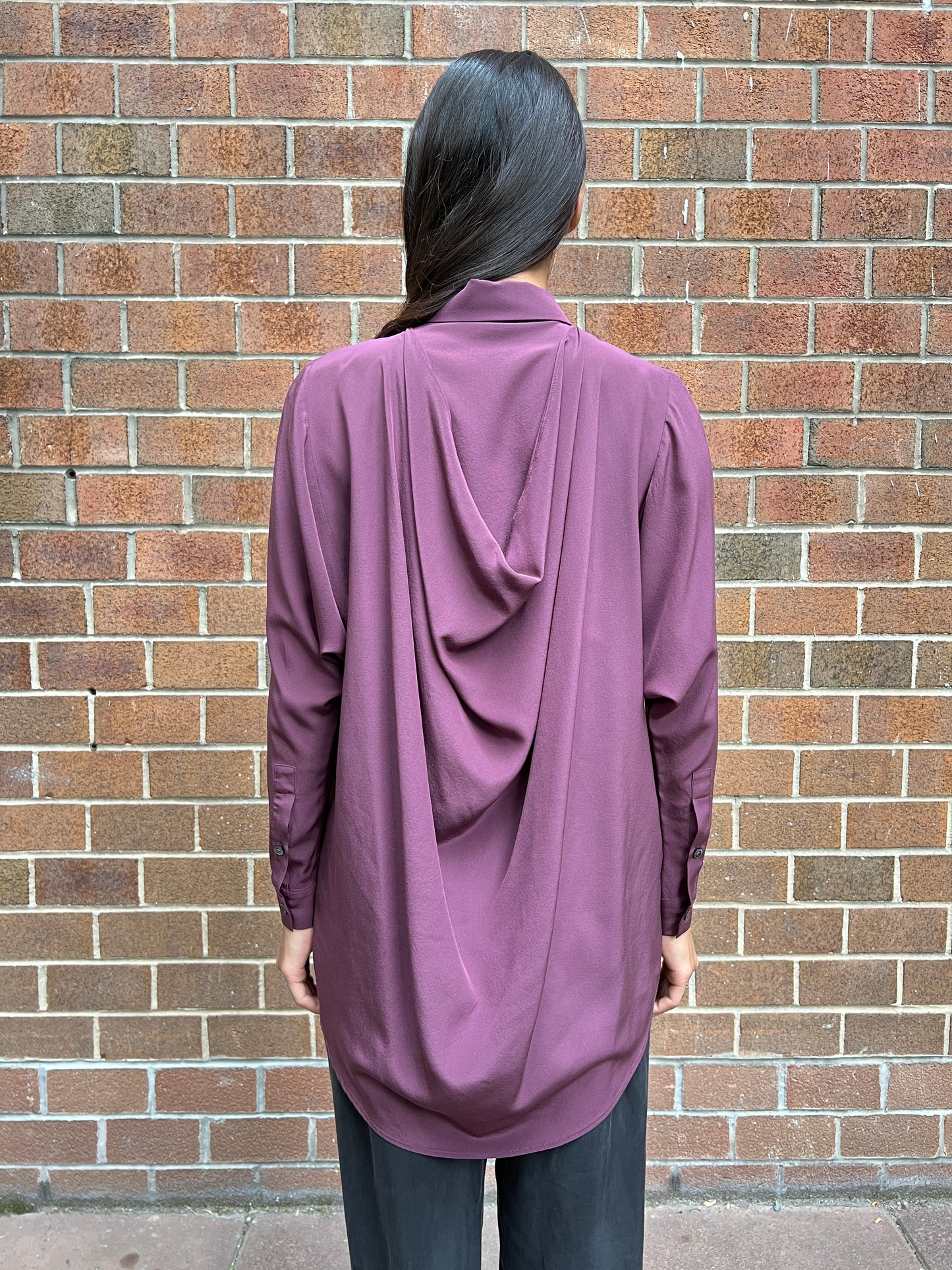Back of woman wearing lilac silk shirt with a draped back and deep kimono-style armhole untucked untucked
