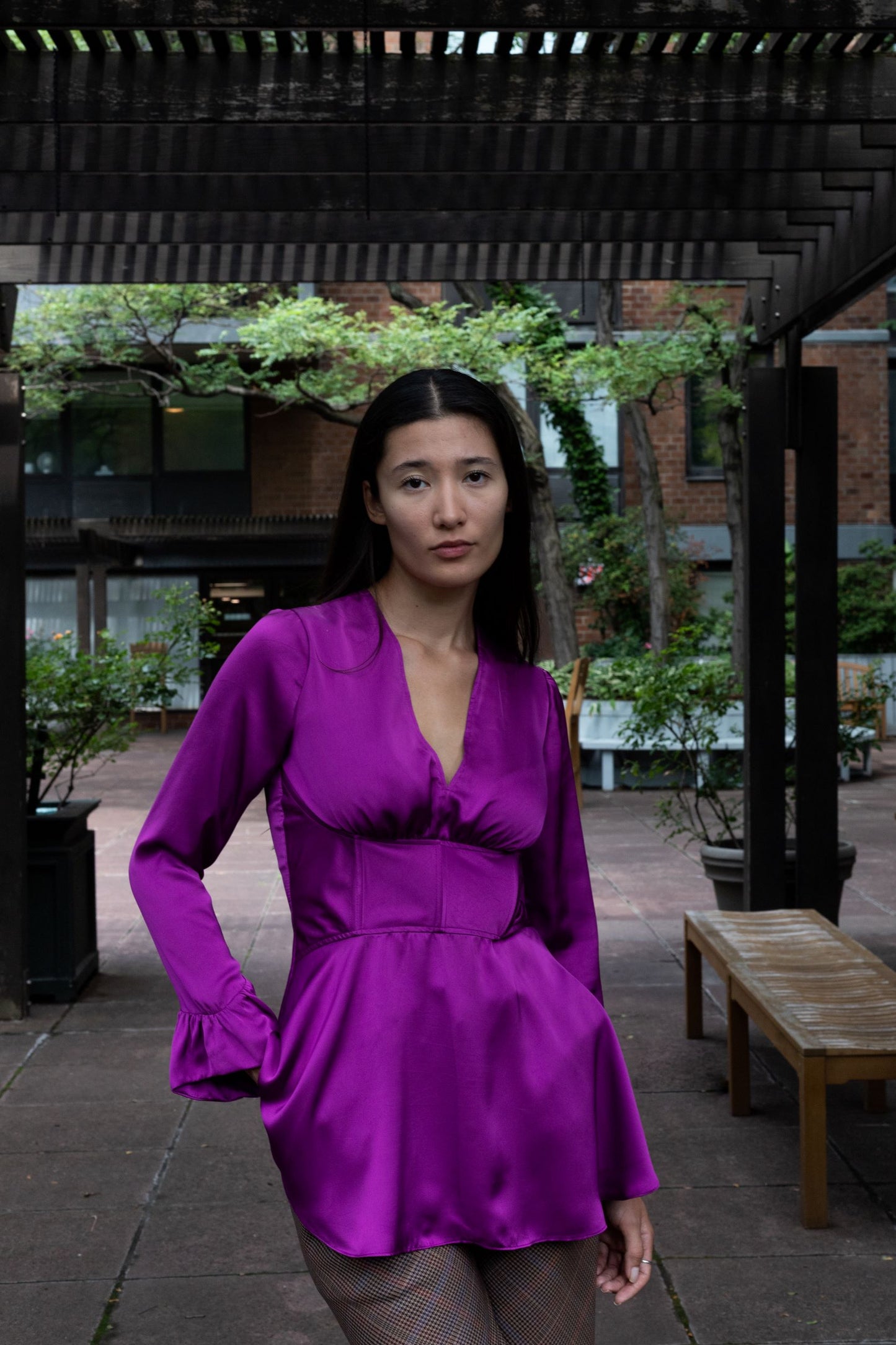 Woman wearing a purple cupro corset blouse and skirt and fringed sleeves over plaid pants