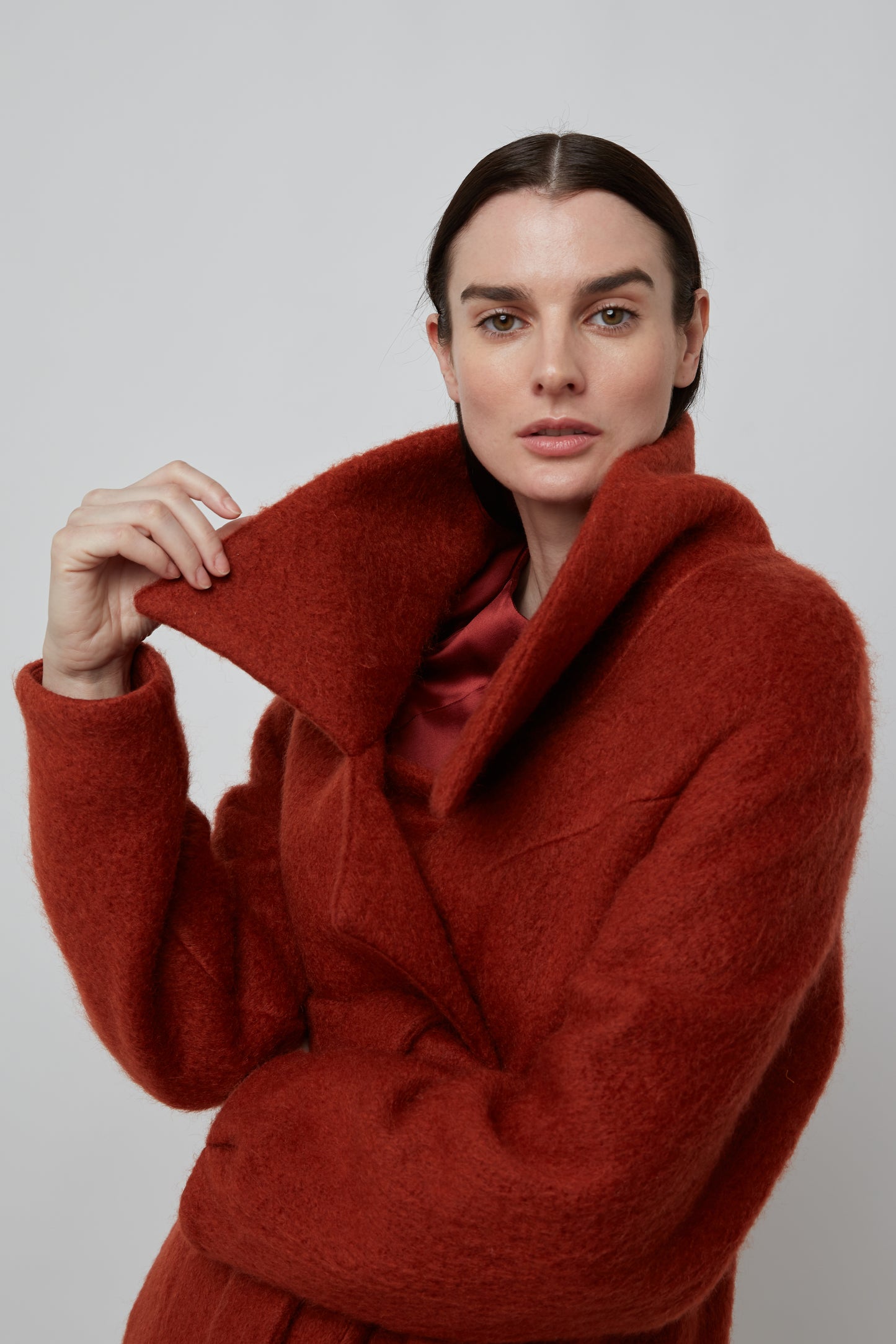 Woman wearing a rust colored mohair double breasted coat with wide collar cut and double self tie belt