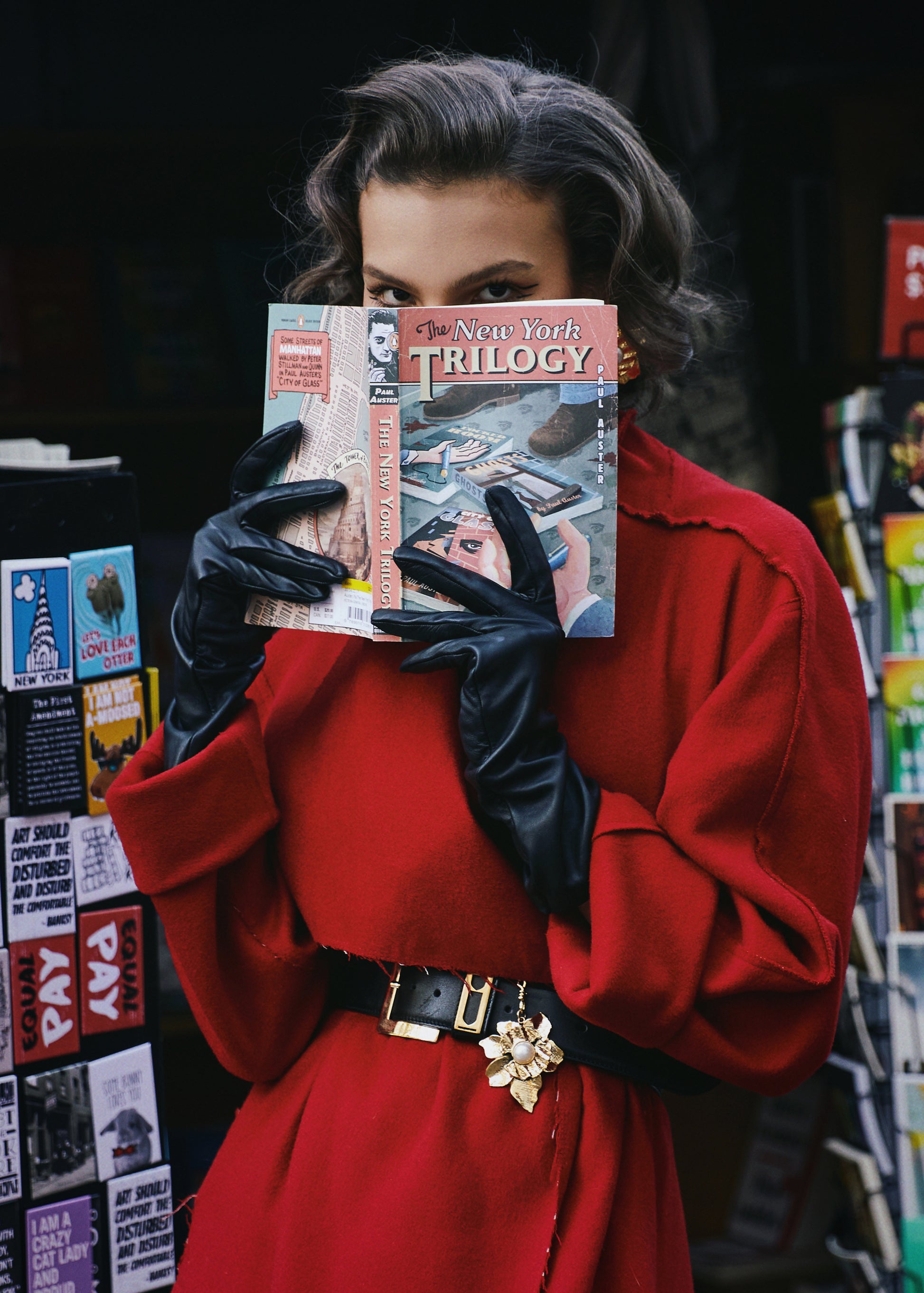 A woman wearing a red rumi coat with a black-golden accented waist belt. She is concealing her lower face with only her eyes exposed with a book.

By @monicabaddar
Featuring our Rumi coat
Modeled by @savka.dm
Styled by @styledbybruce
Hair by @michikoboorberg
Make up @brennadmakeup
Courtesy @the_confessional_showroom_nyc