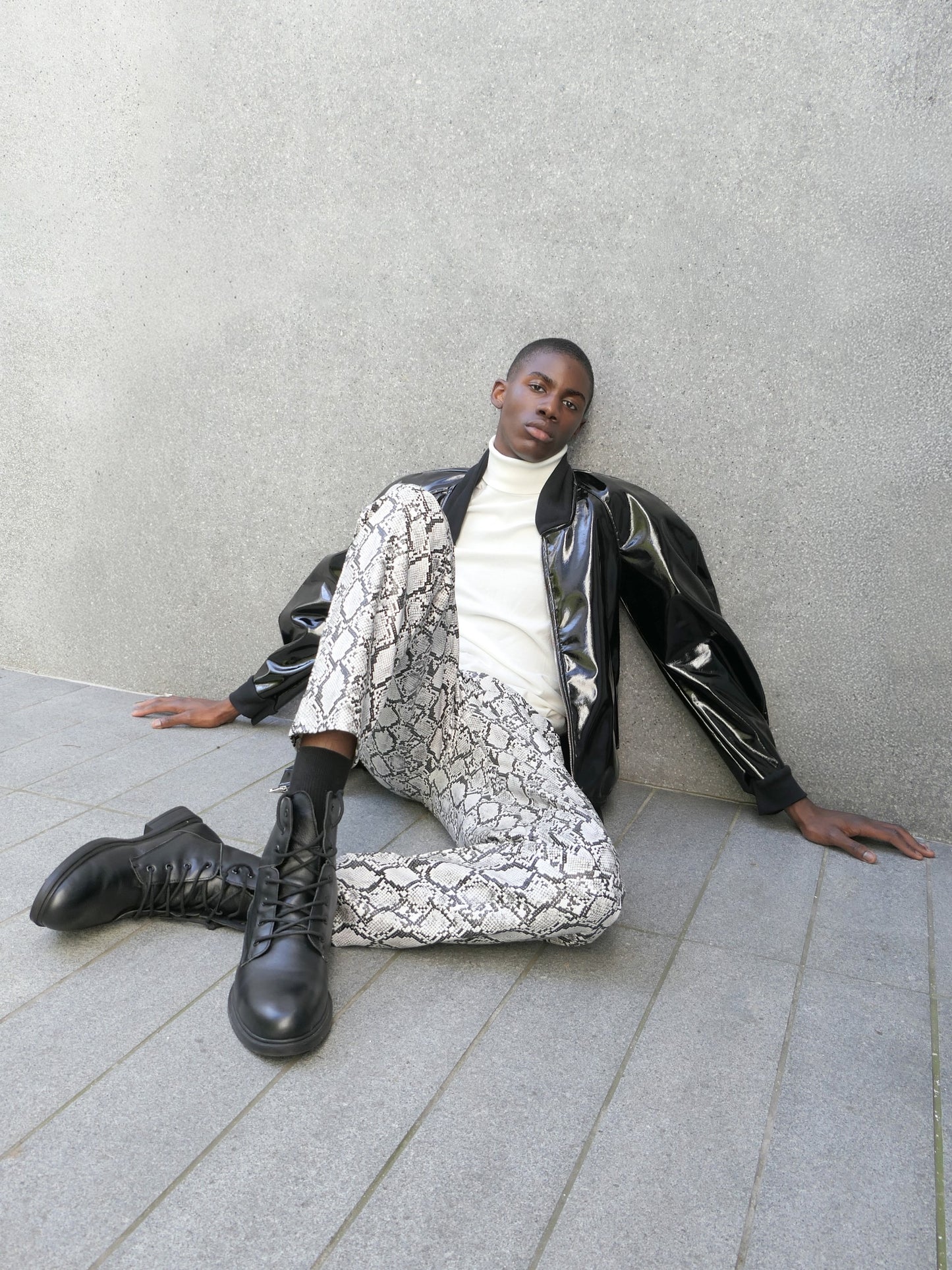 A man wearing a patent barrel sleeved jacket sitting on the floor with white geometric pattern pants and black combat boots.

Credits:
Photographer/Stylist: Nikko Kefalas @nikkokefalas
Jacket: @heike_ny