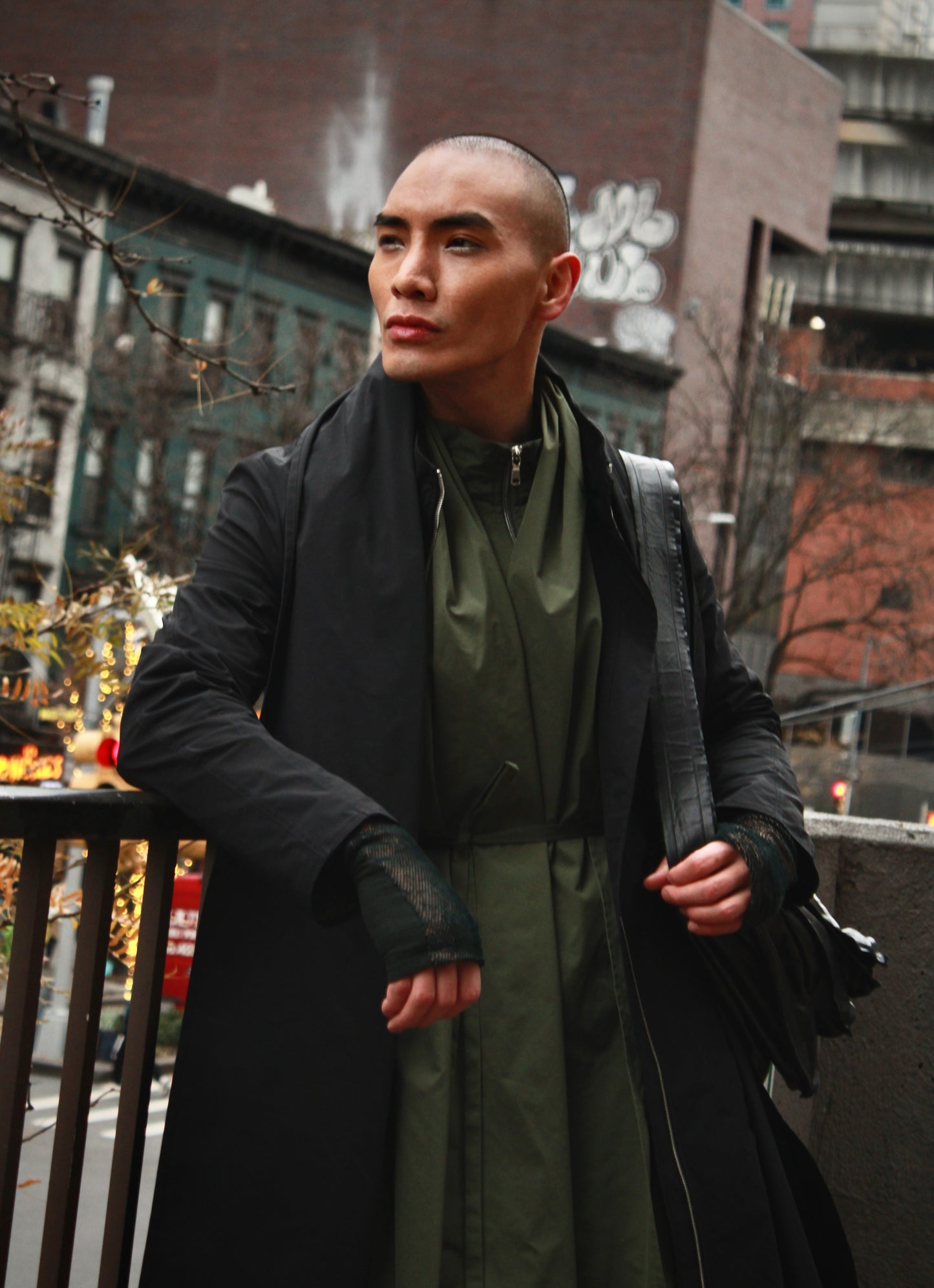 Person in an outdoor urban environment leaning on a balcony fence. Wearing black Japanese nylon raincoat and looking away.

Model: @lejamie_