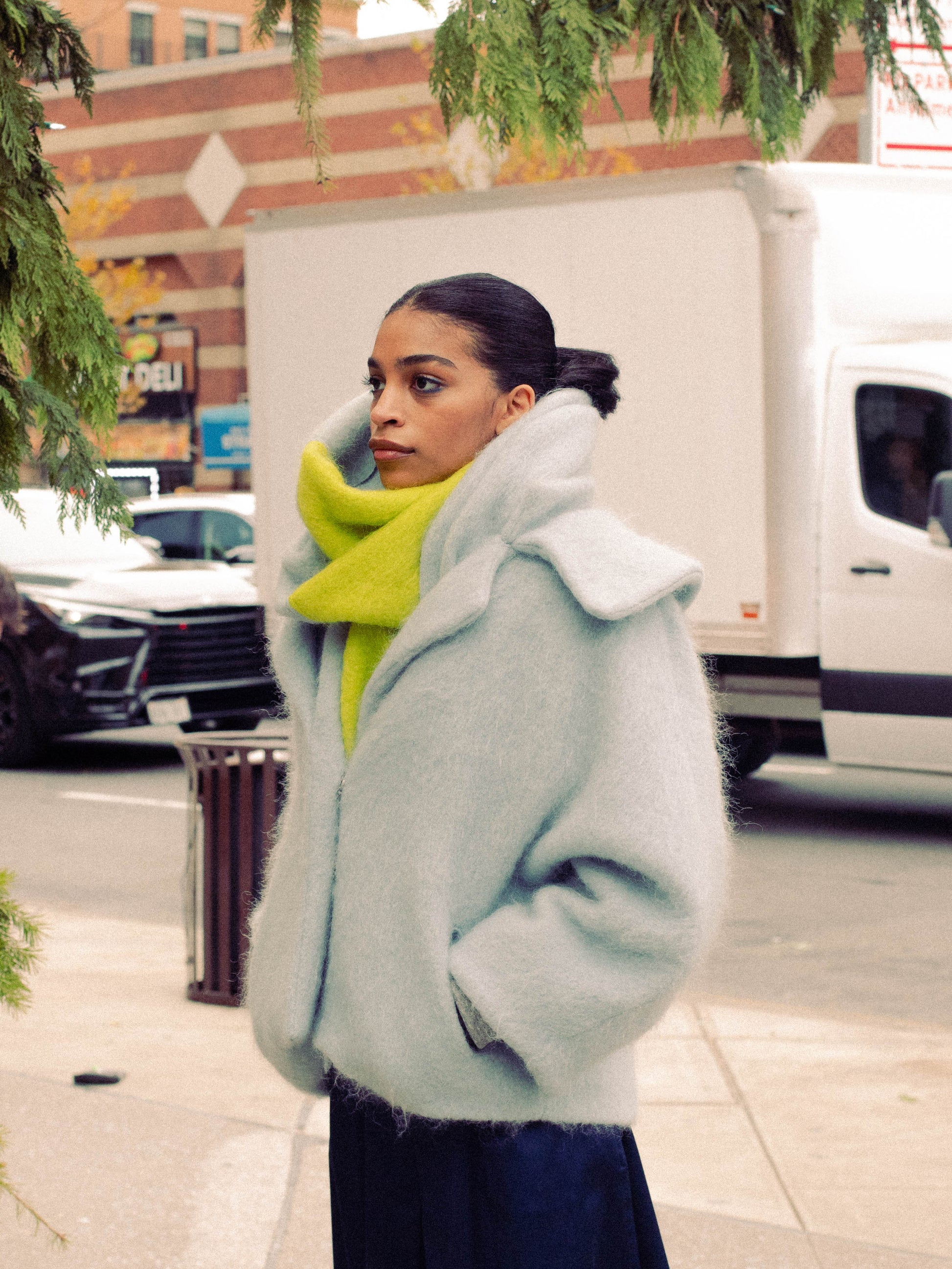 Woman wearing a sky blue alpaca jacket with a navy dress standing on a sidewalk.