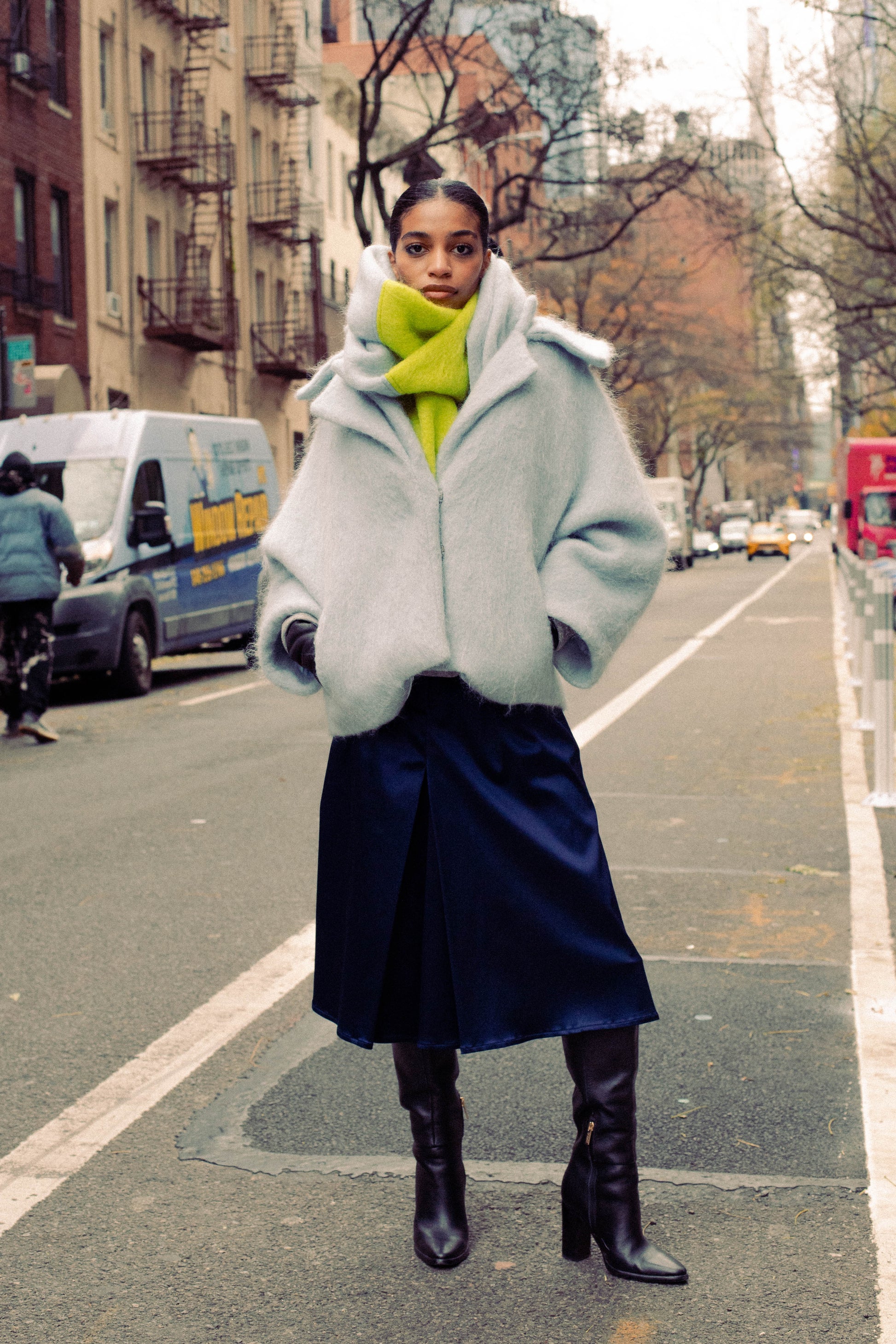 Woman wearing a sky blue alpaca jacket with a navy dress standing in the middle of a street.
