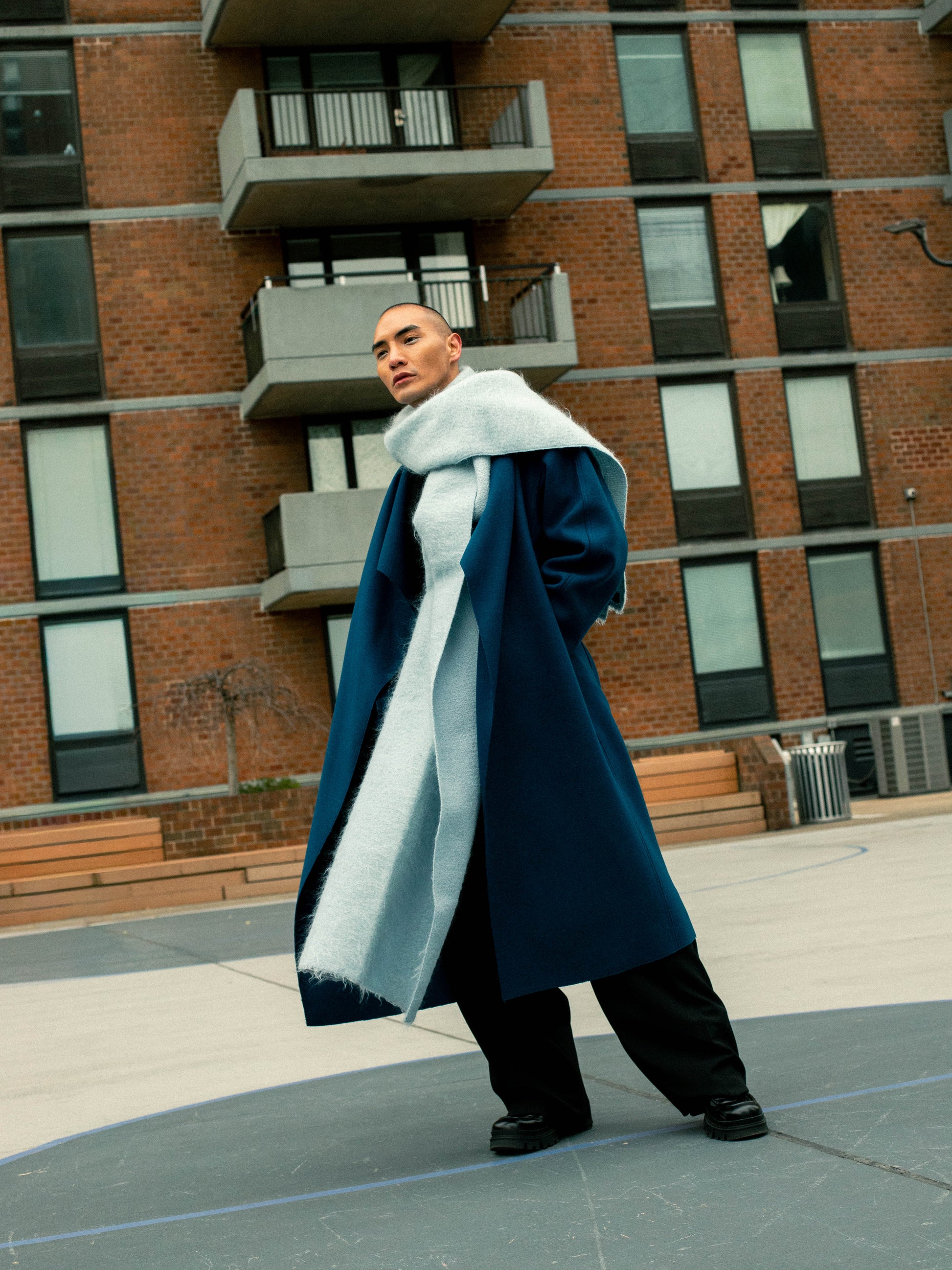 A person wearing a white scarf, acting as an outer layer for the blue rumi coat. Standing in front of an apartment building.

Model: @lejamie_