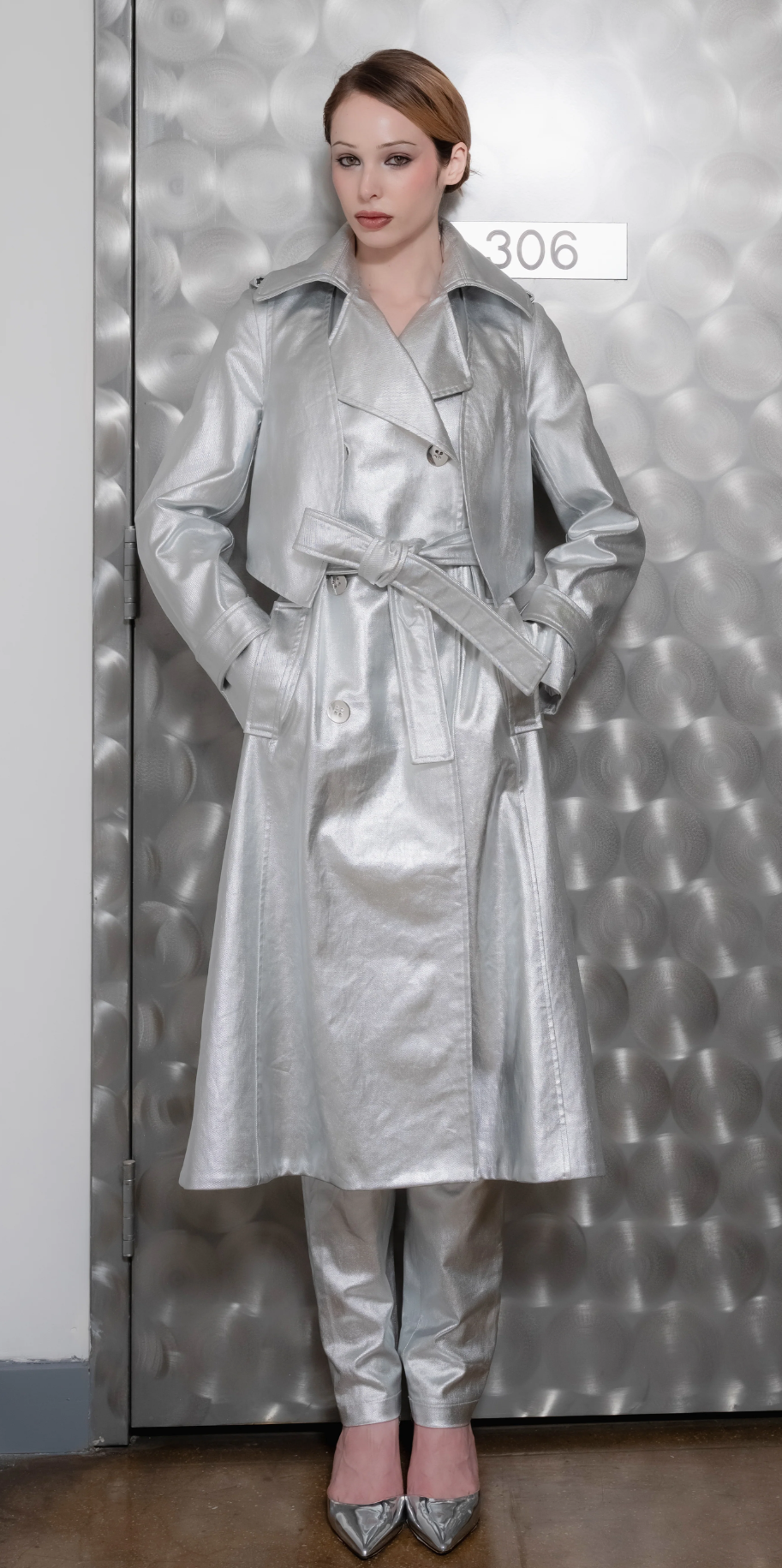 A woman wearing a Long Silver Bristol Trench coat made of satin with a removable vest in textured leather in front of a metallic door.

@natalieturnerr captured beautifully by @_vazhak_ creative eye @kent.nycfashion
@makohairmakenyc
@gabriel.barse
@suecandia
@the_confessional_showroom_ny
@confessional_showroom_miami