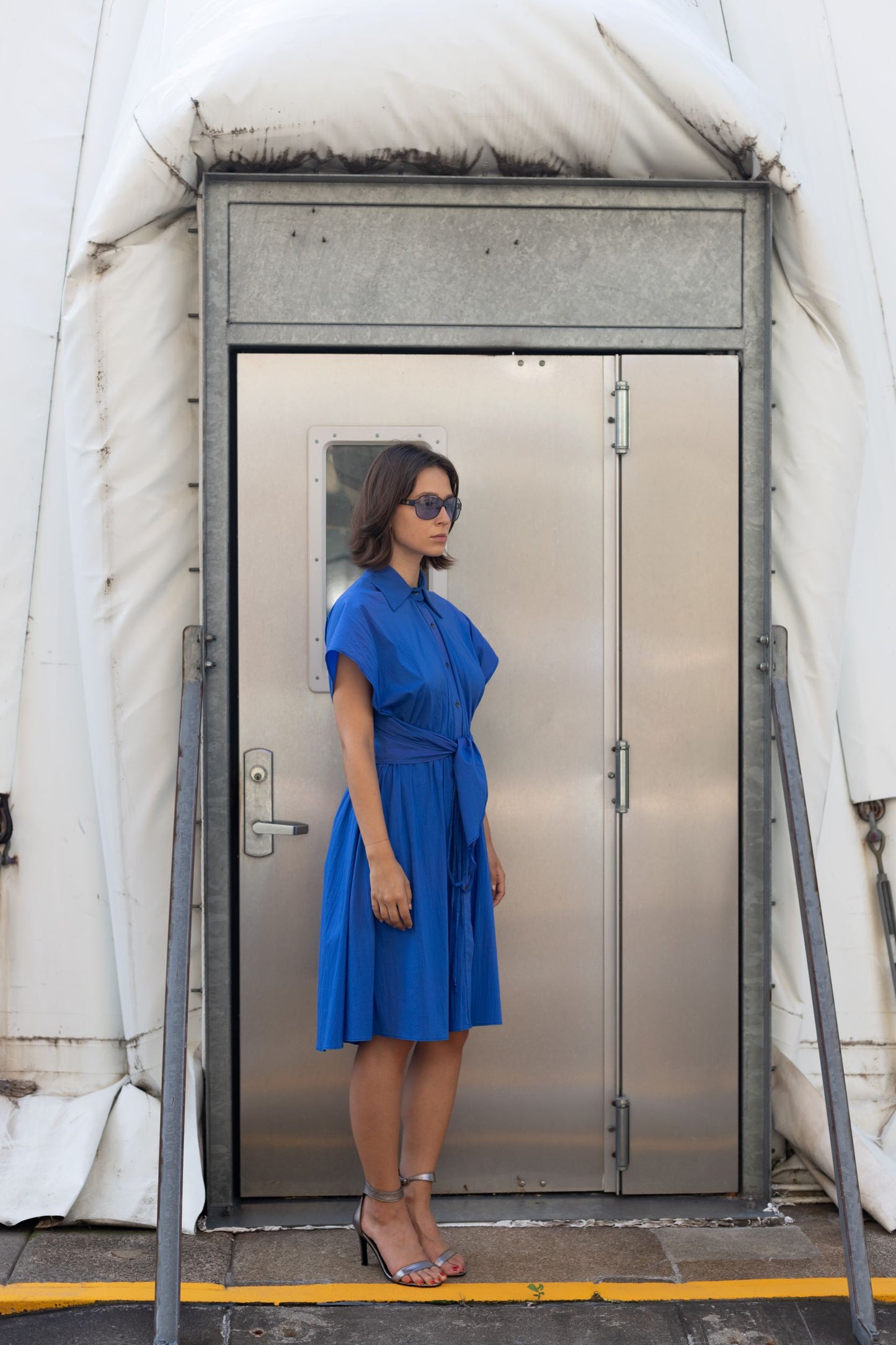 Woman wearing a cupro dress in cobalt blue with button detailing and adjustable waist styled as belt
