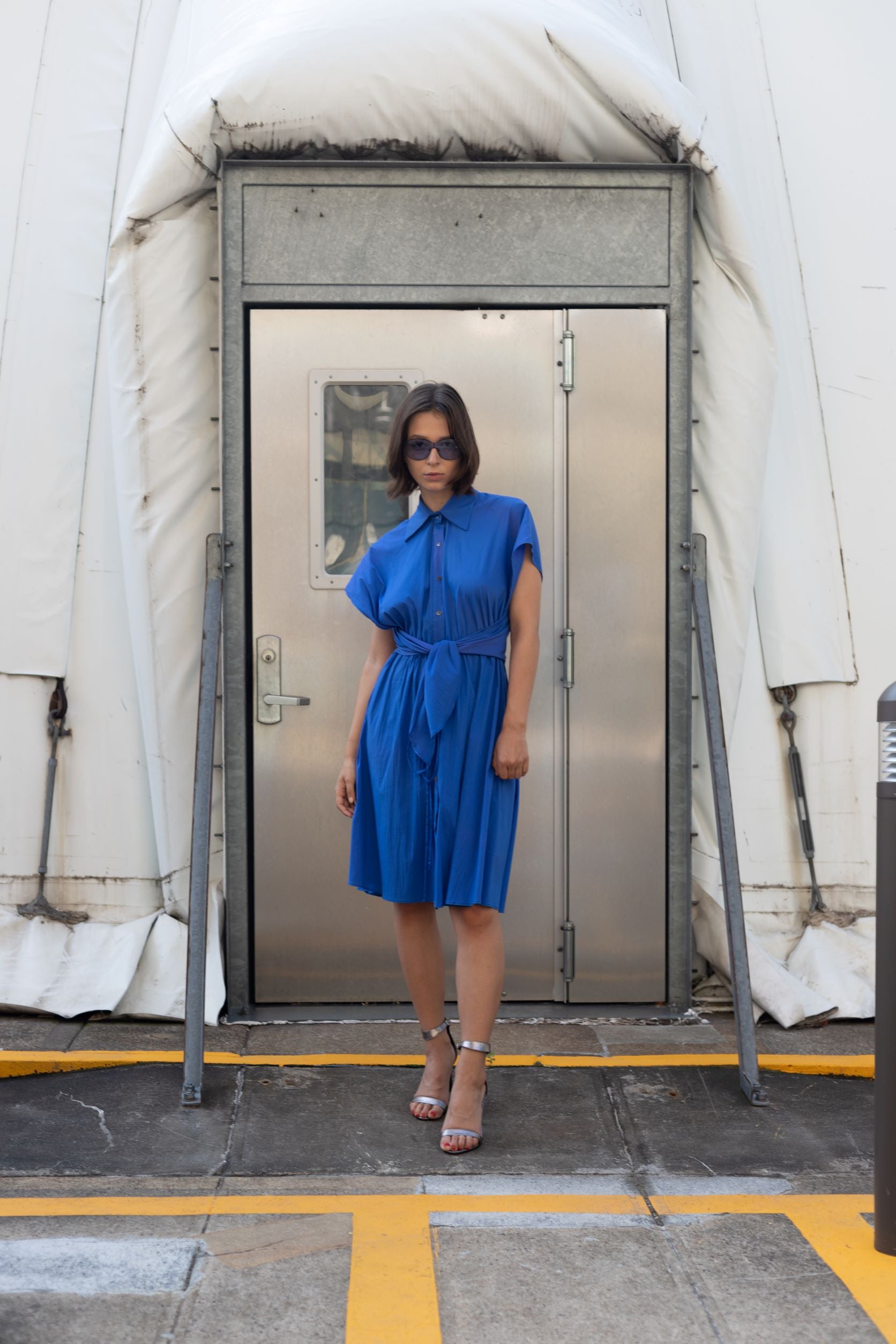 Woman wearing a cobalt blue cupro dress with button detailing and adjustable waist styled as belt